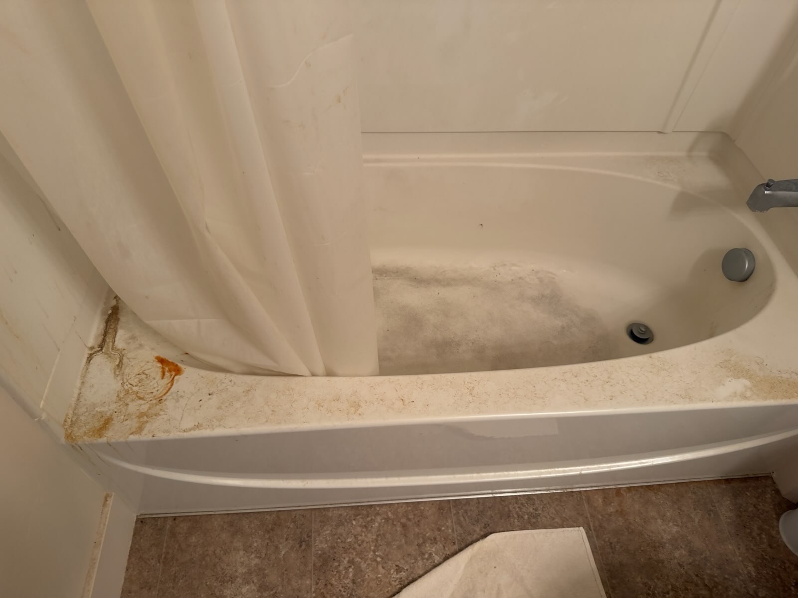 Bathtub with rust stains on rim and grime in basin before cleaning